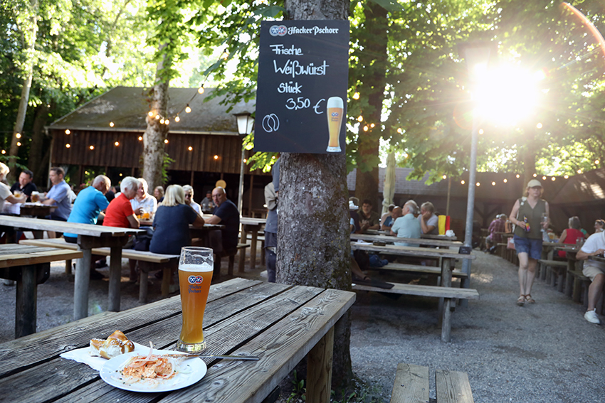 Weissbier and food on a wooden beer garden table with guests and warm evening sunlight behind