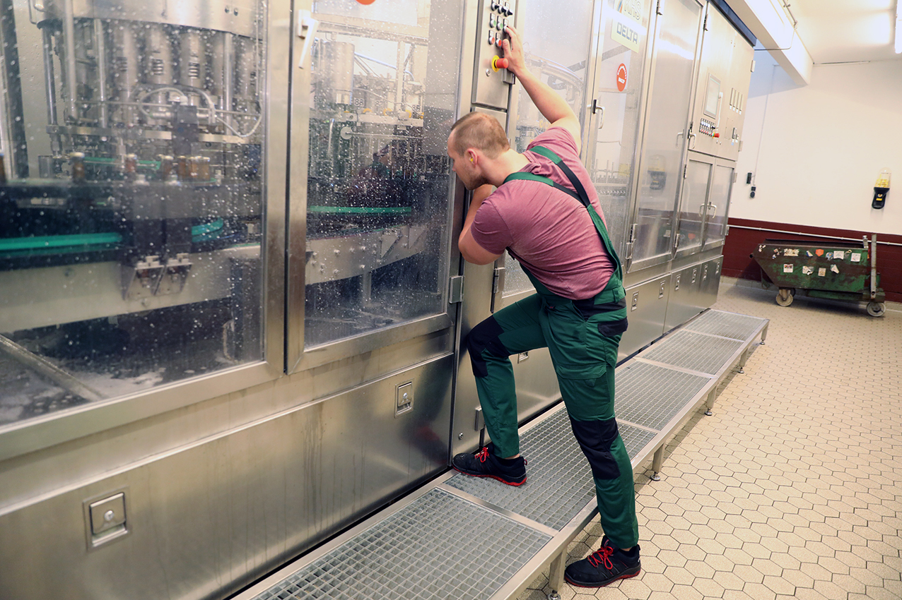 A Barre brewery worker in green overalls operating the controls of a stainless steel brewing machine