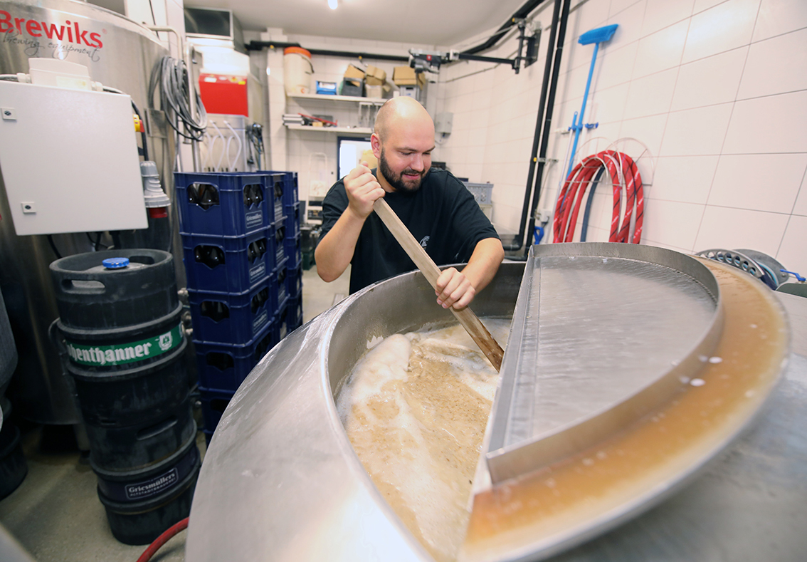 A brewer stirring the mash with a wooden paddle