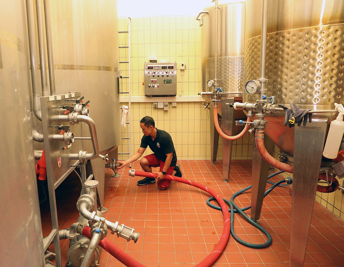 A brewer connecting a hose to a stainless steel fermentation tank