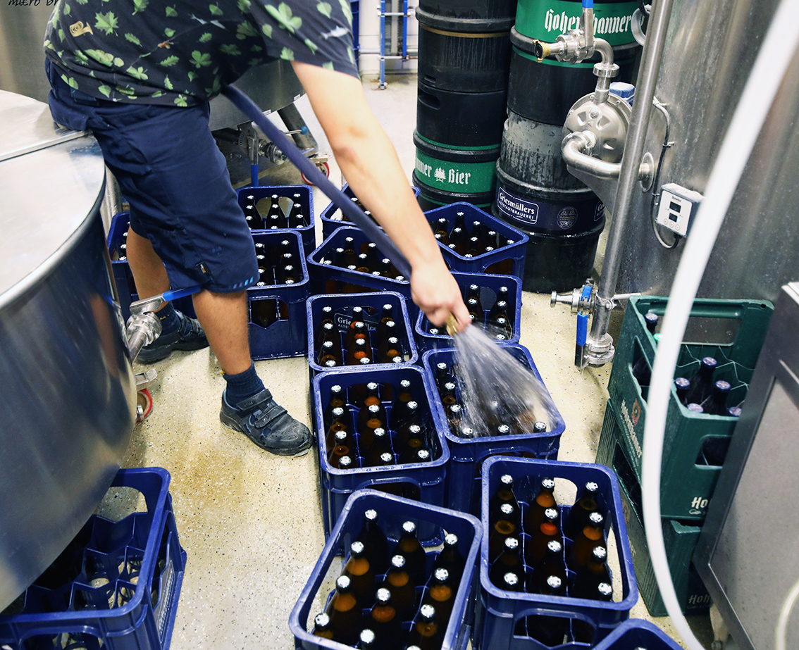 A brewer hosing down crates of freshly filled bottles on the brewery floor