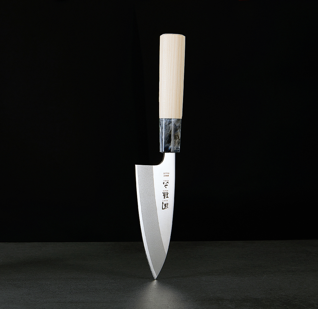 Japanese chef's knife with pale wooden handle balancing on its tip against a dark backdrop