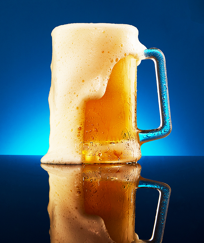 Overflowing beer stein with cascading foam captured against a deep blue backdrop