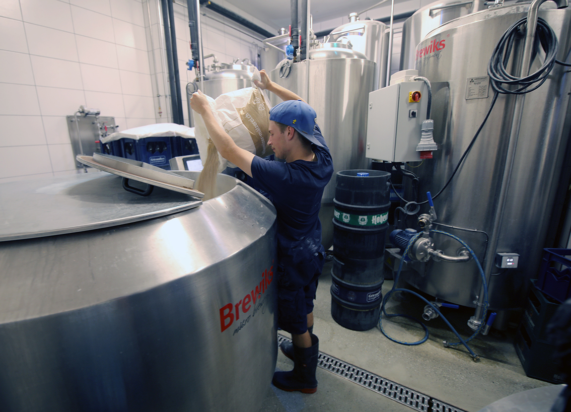 A brewer emptying a sack of grain into the open mash tun
