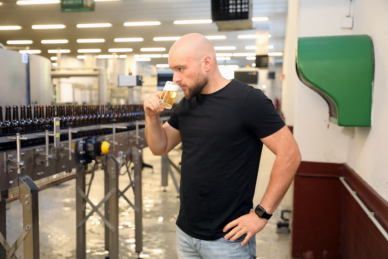 A brewer tasting a freshly drawn glass of beer beside the bottling line
