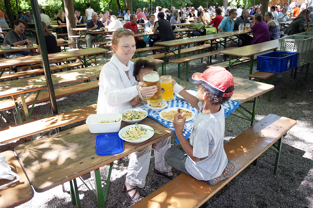 Woman toasting with a child at a beer garden table set with two beers and food