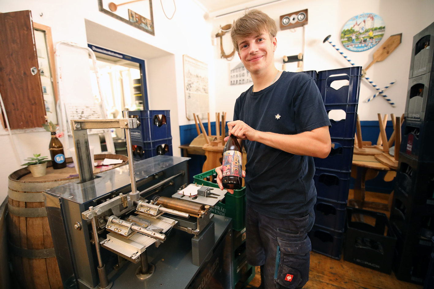 A young brewer holding a freshly labelled bottle beside the labelling machine