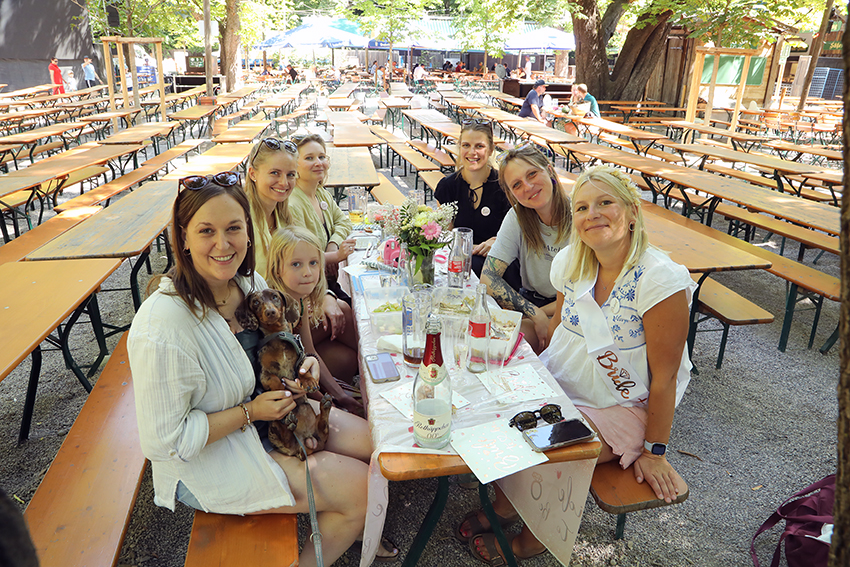 Group of women sitting together at a beer garden table surrounded by empty benches and trees