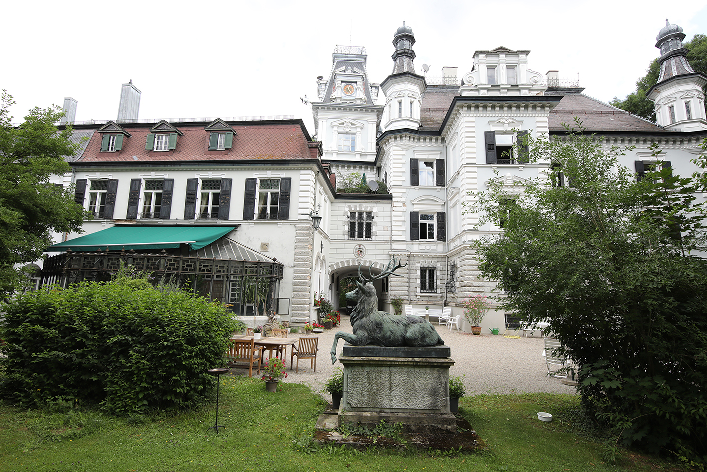 The white baroque facade of Schloss Au with a bronze stag statue in the garden