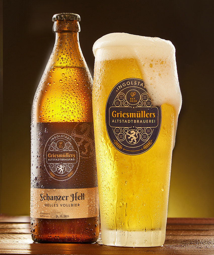 A bottle of Schanzer Hell beside a full, freshly poured glass with a thick head of foam