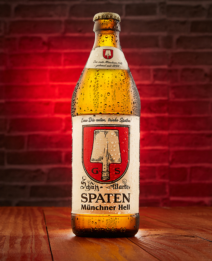 Spaten Münchner Hell bottle on a wooden table against a warm red brick wall