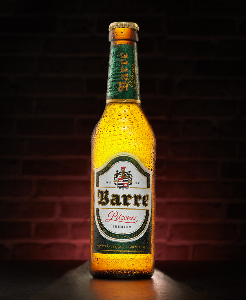 Barre Pilsener bottle with condensation against a dark brick wall with warm reflection