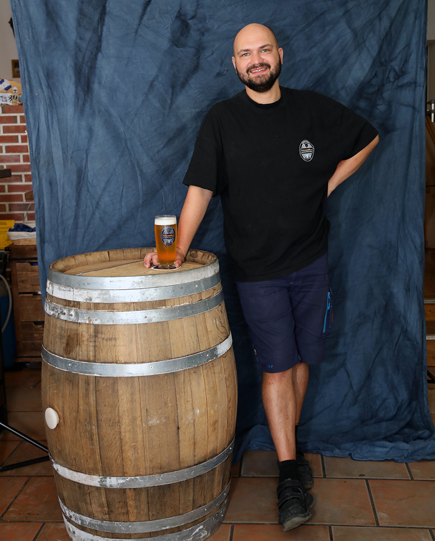 The head brewer standing beside a wooden barrel with a glass of beer