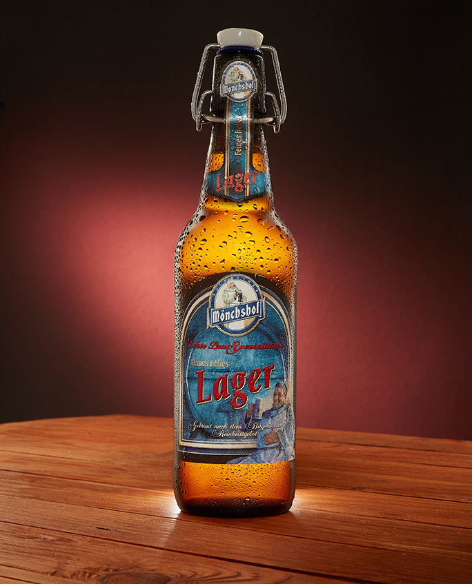 Mönchshof swing-top Lager bottle on a wooden table with warm red glow