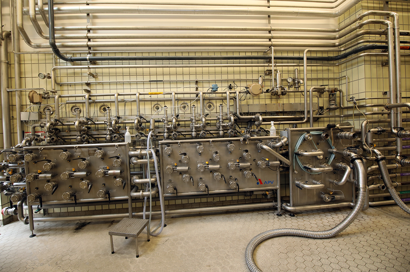 Stainless steel brewing machinery with pipes, valves and gauges in a tiled brewhouse