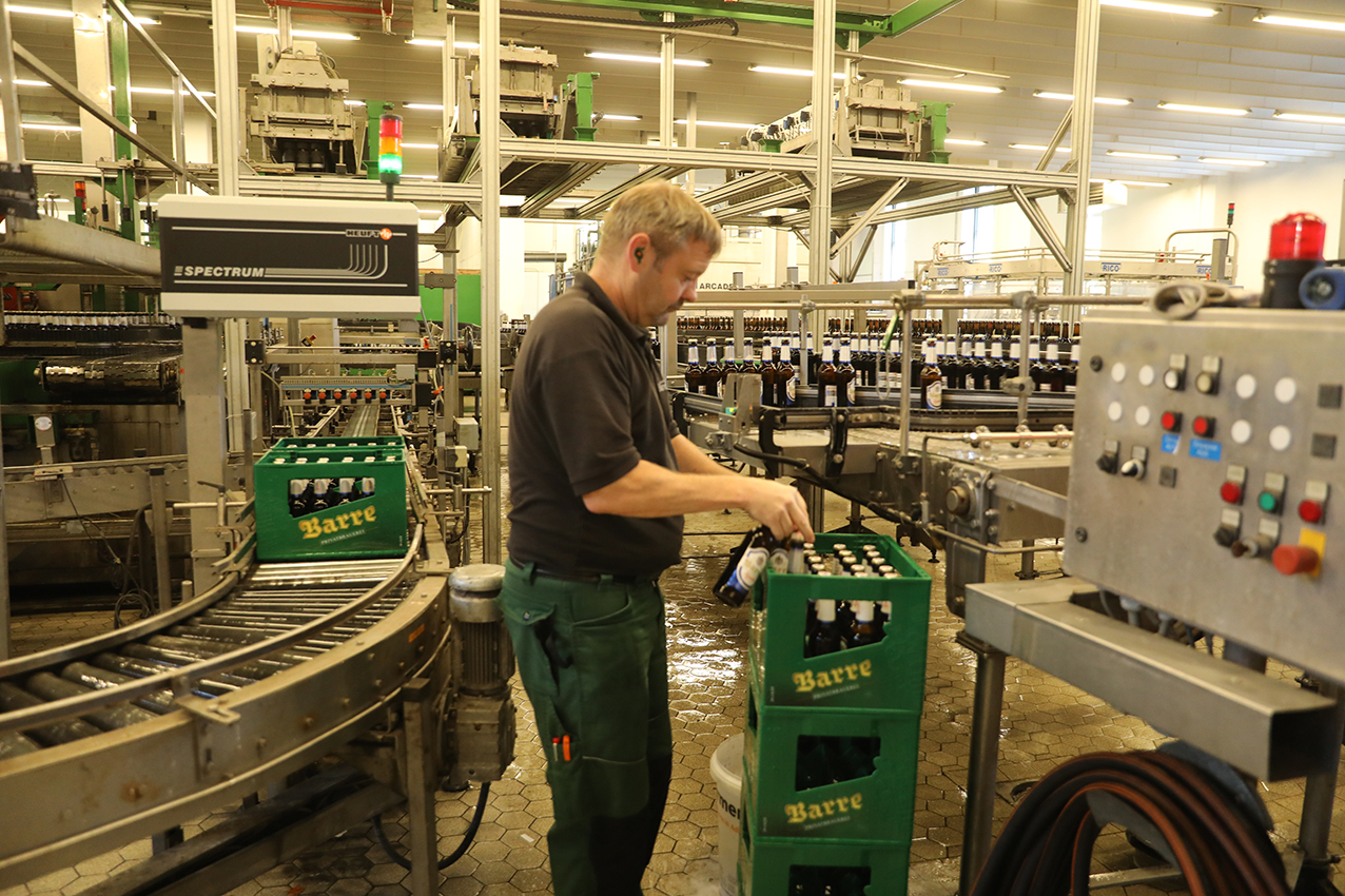 A worker packing filled bottles into green Barre crates at the line