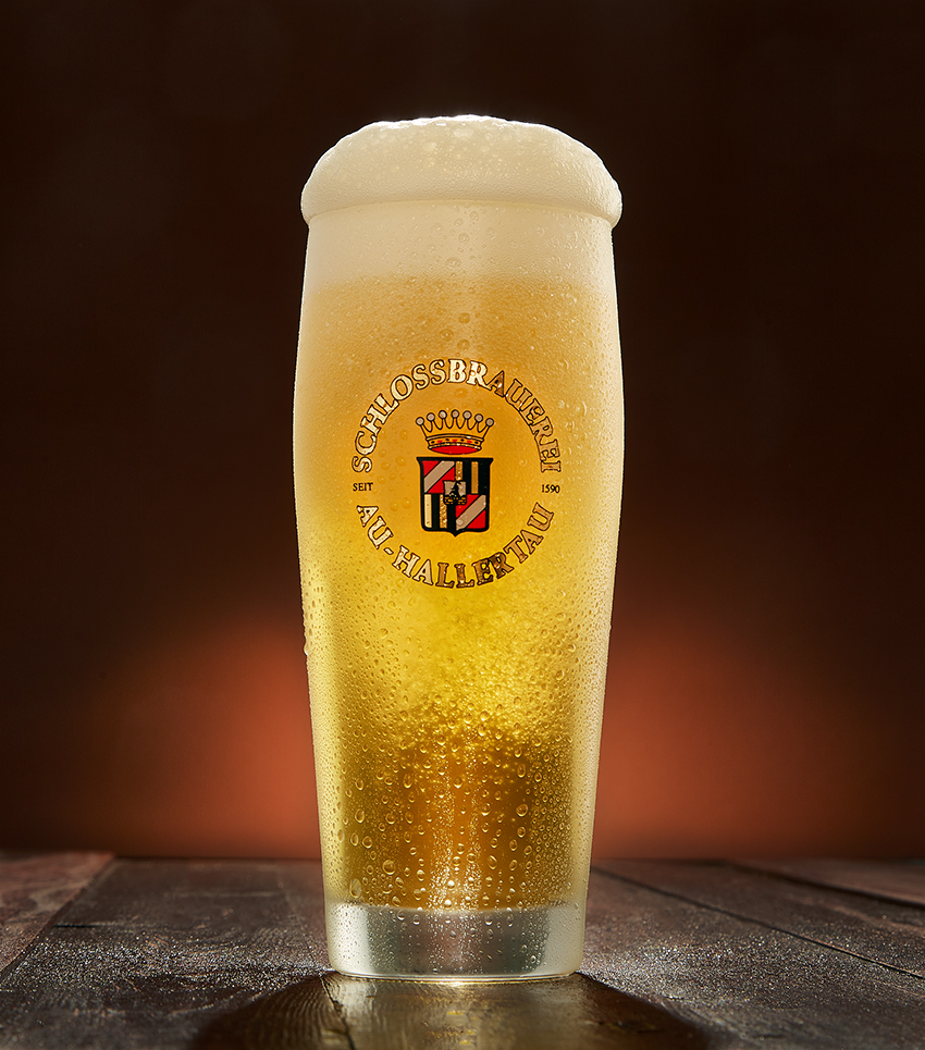 A tall glass of Auer Helles with the Schlossbrauerei Au-Hallertau logo and a creamy head
