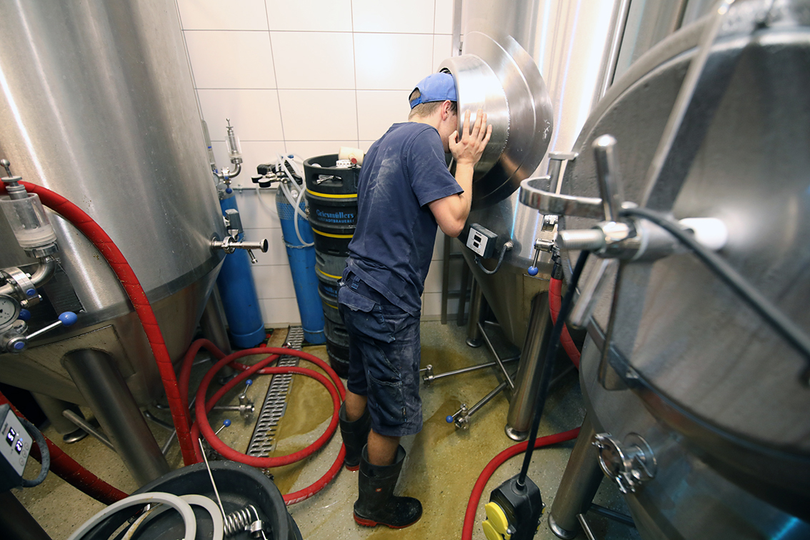 A young brewer cleaning inside an open fermentation tank