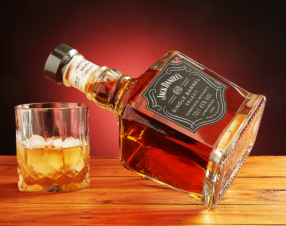 Jack Daniel's bottle with a whisky tumbler over ice on wood