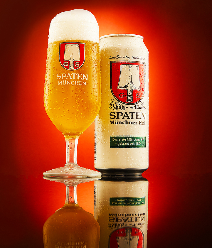 Spaten München goblet and can paired on a reflective surface with a warm red glow