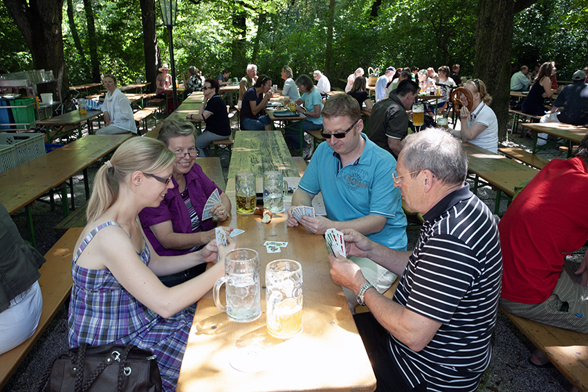 Group of people playing cards at a beer garden table with beer glasses in the sunlight