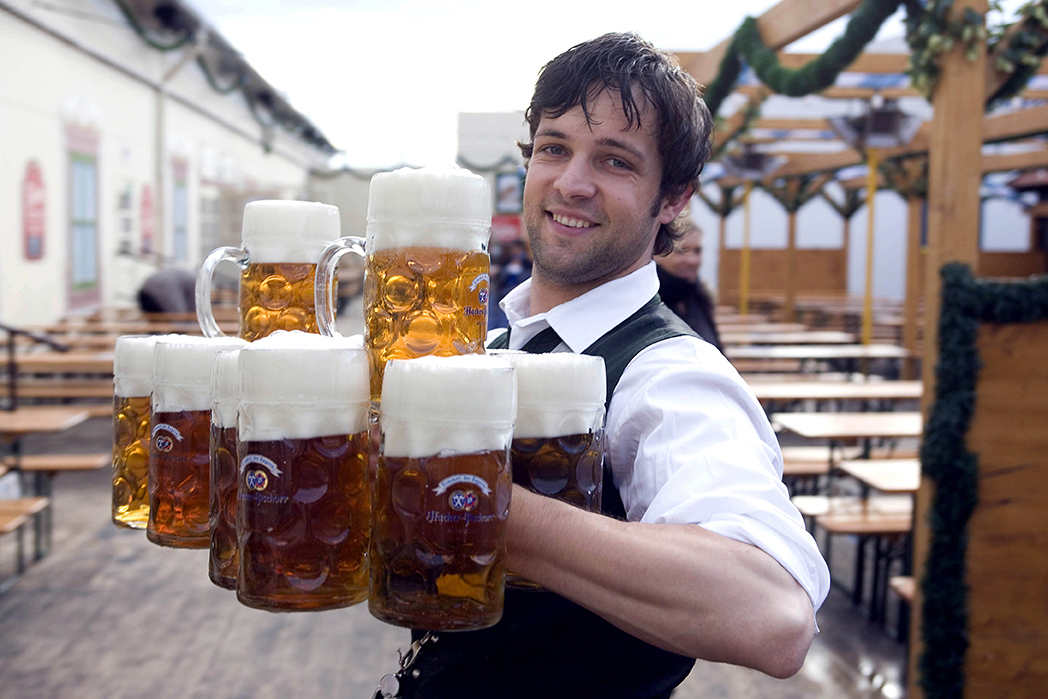 A smiling server in traditional dress holding eight full beer steins