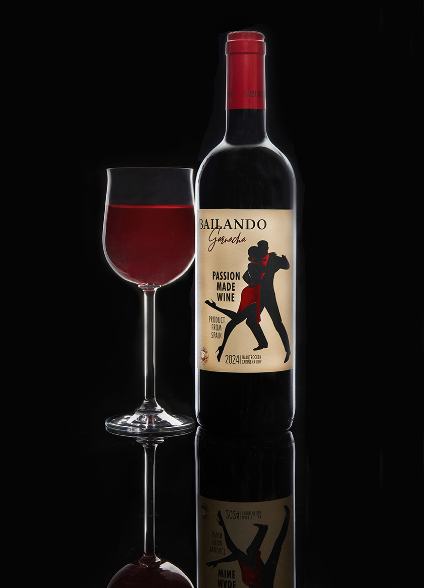 A Bailando Garnacha bottle beside a filled wine glass on a black reflective surface