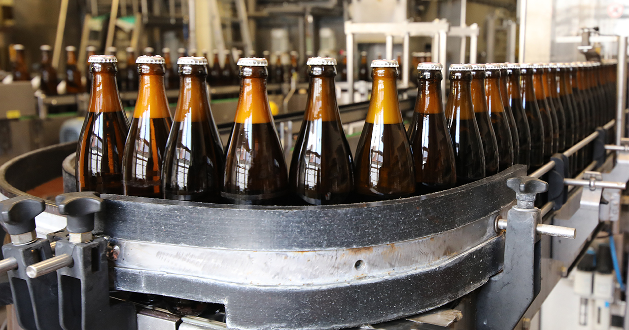 Close-up of filled brown beer bottles moving along the conveyor after capping