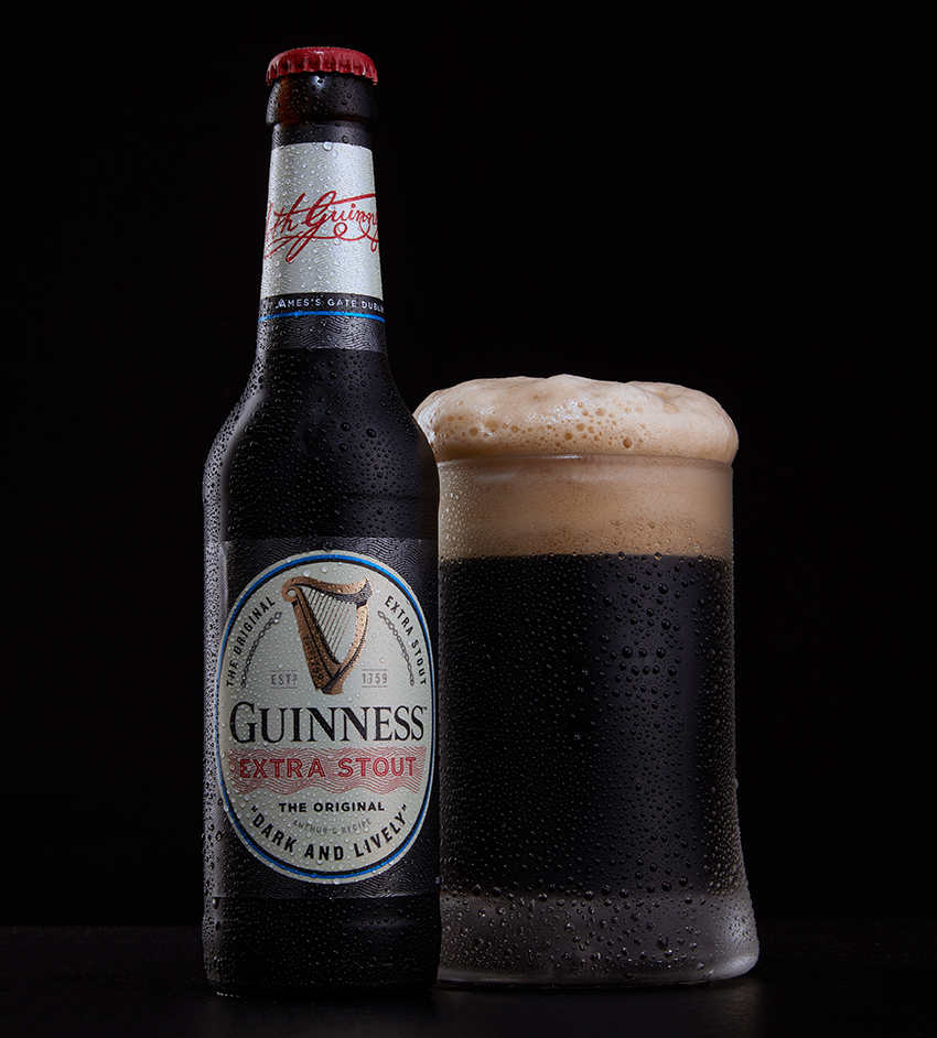 Guinness Extra Stout bottle beside a full pint glass with a creamy head