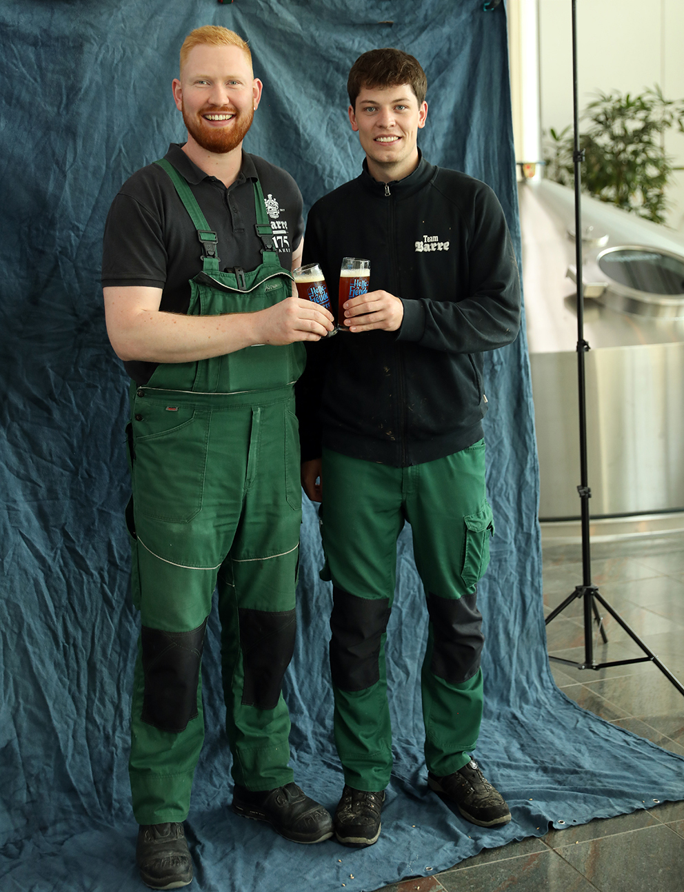 Two Barre brewers raising their glasses together in front of a blue backdrop