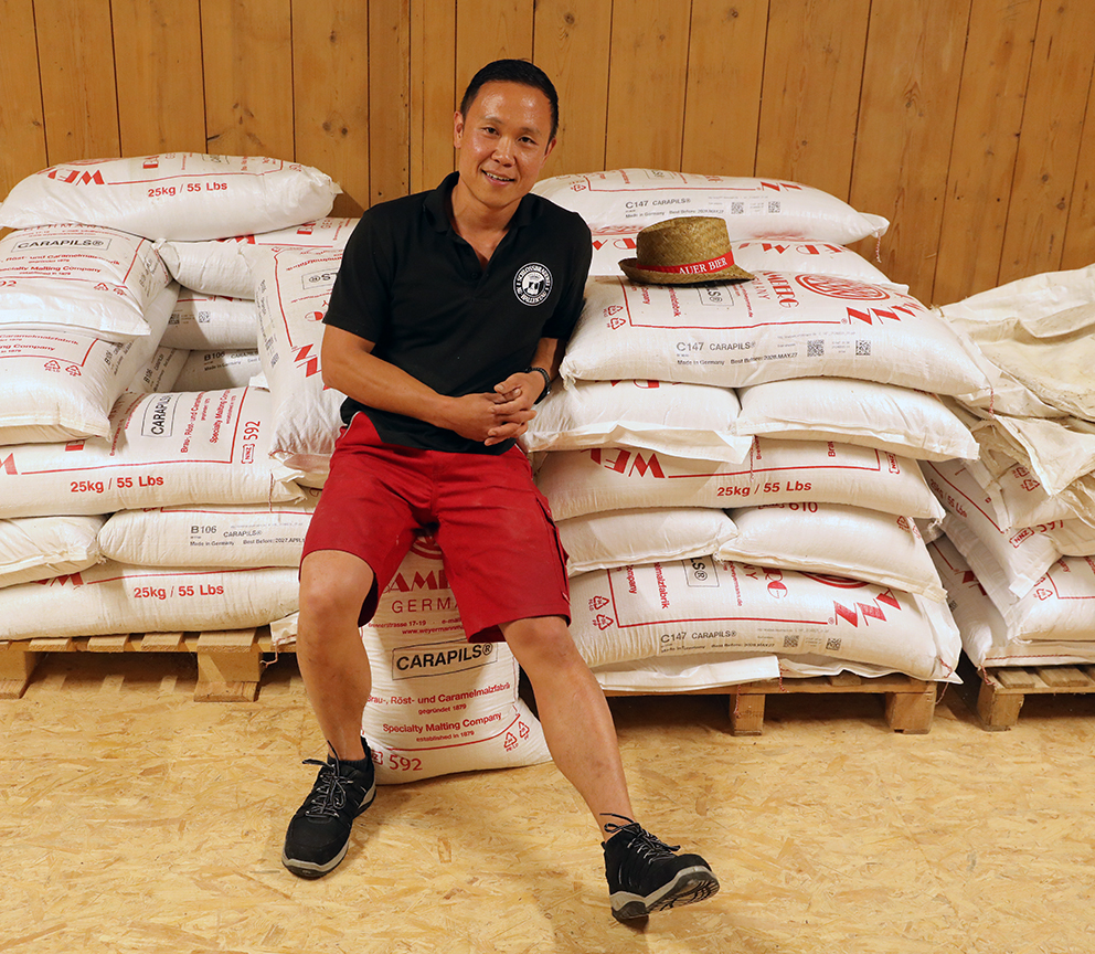 A brewer seated among stacked sacks of Carapils malt in the malt store