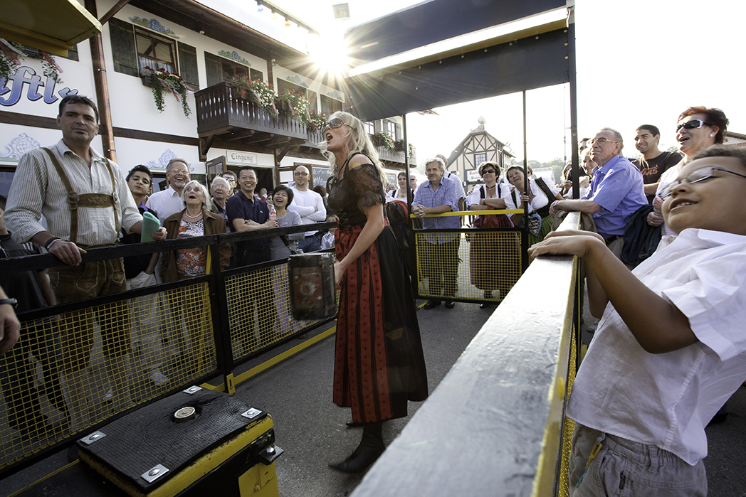 A singer performing on a festival wagon as a crowd watches in the evening sun