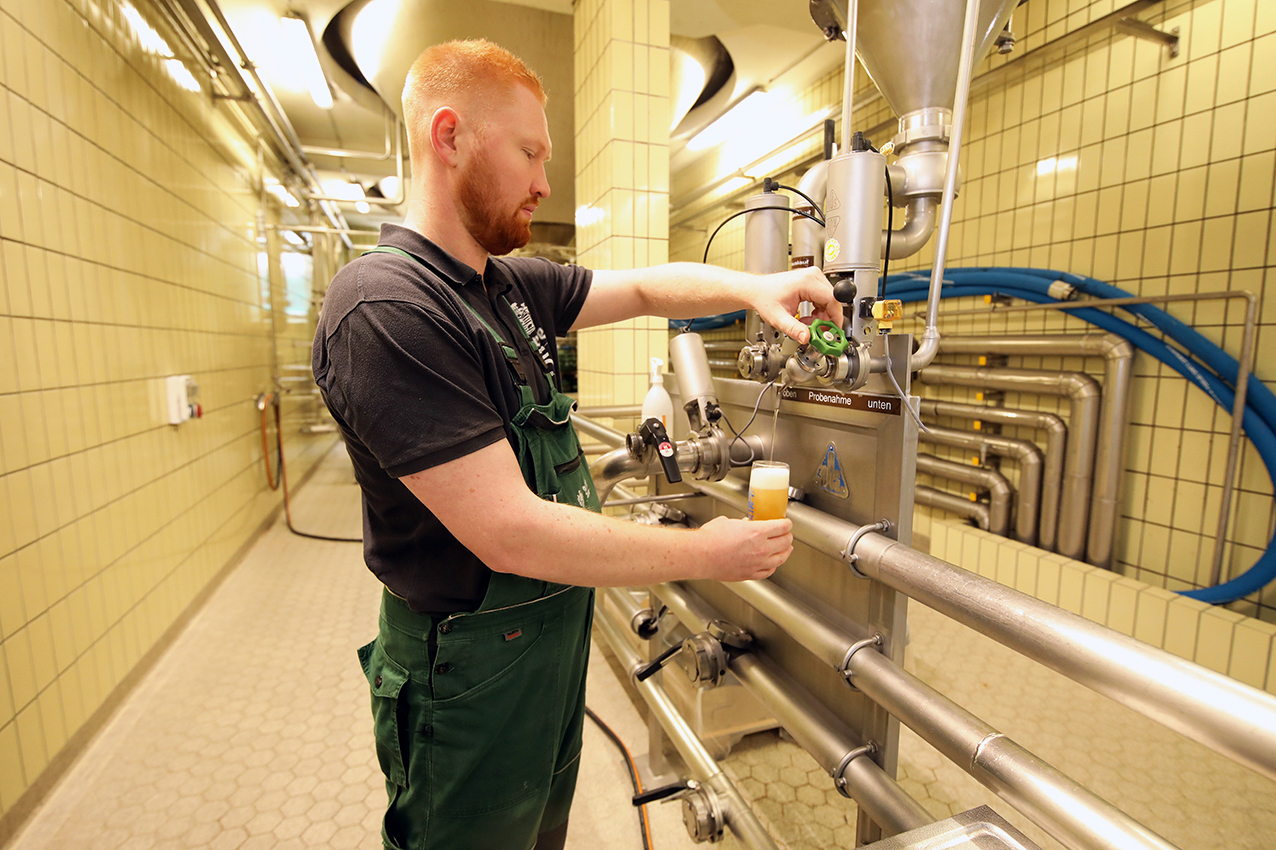 A brewer drawing a sample of beer from the tank valves in the tiled cellar