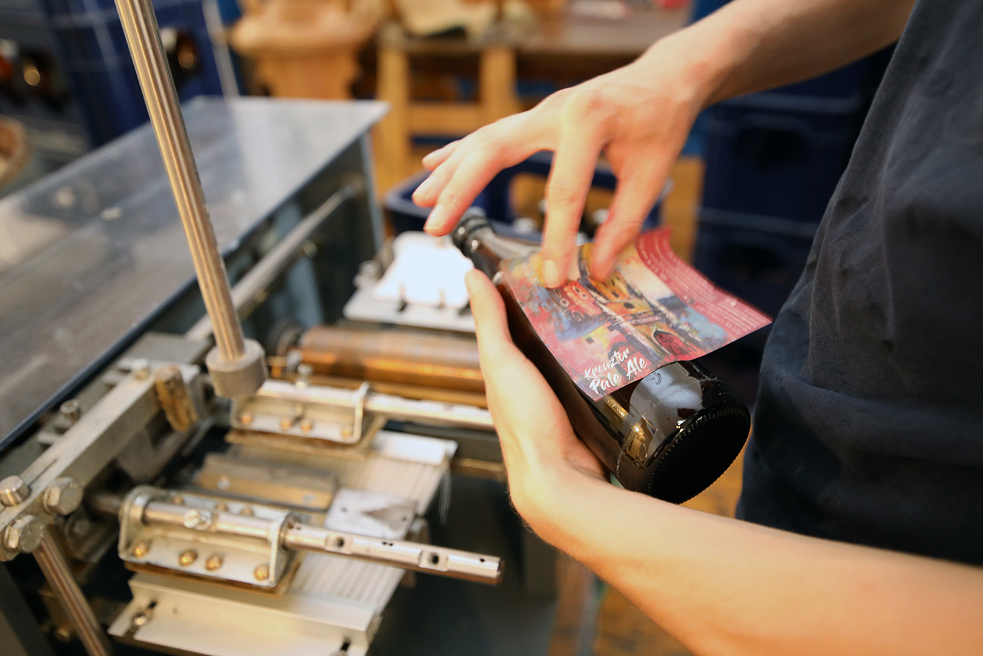 Hands applying a Kreuzter Pale Ale label to a bottle at the old labelling machine