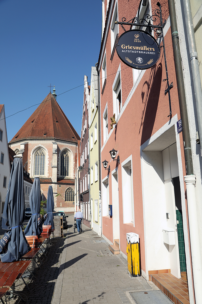 The Griesmüllers Altstadtbrauerei sign hanging over an old town lane beside a church