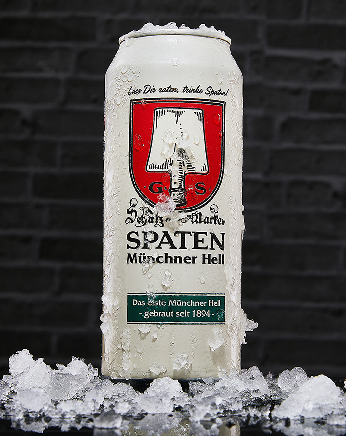 Frosted Spaten Münchner Hell can resting on crushed ice against a dark brick wall