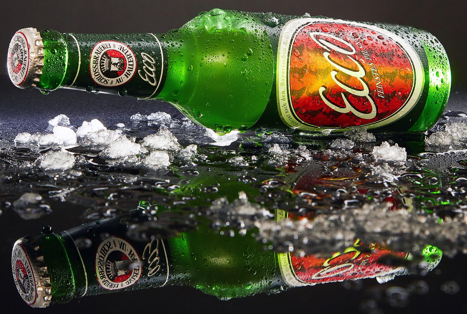 Green Auer beer bottle lying on crushed ice with condensation and reflection
