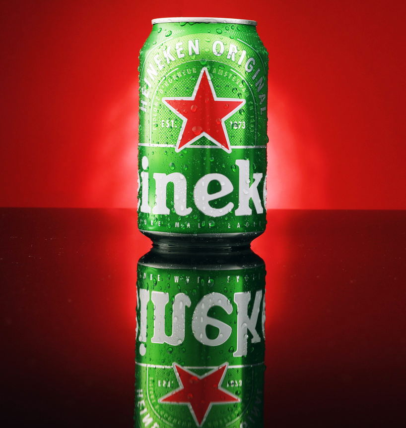 Heineken Original can on a mirrored surface glowing against a crimson red backdrop