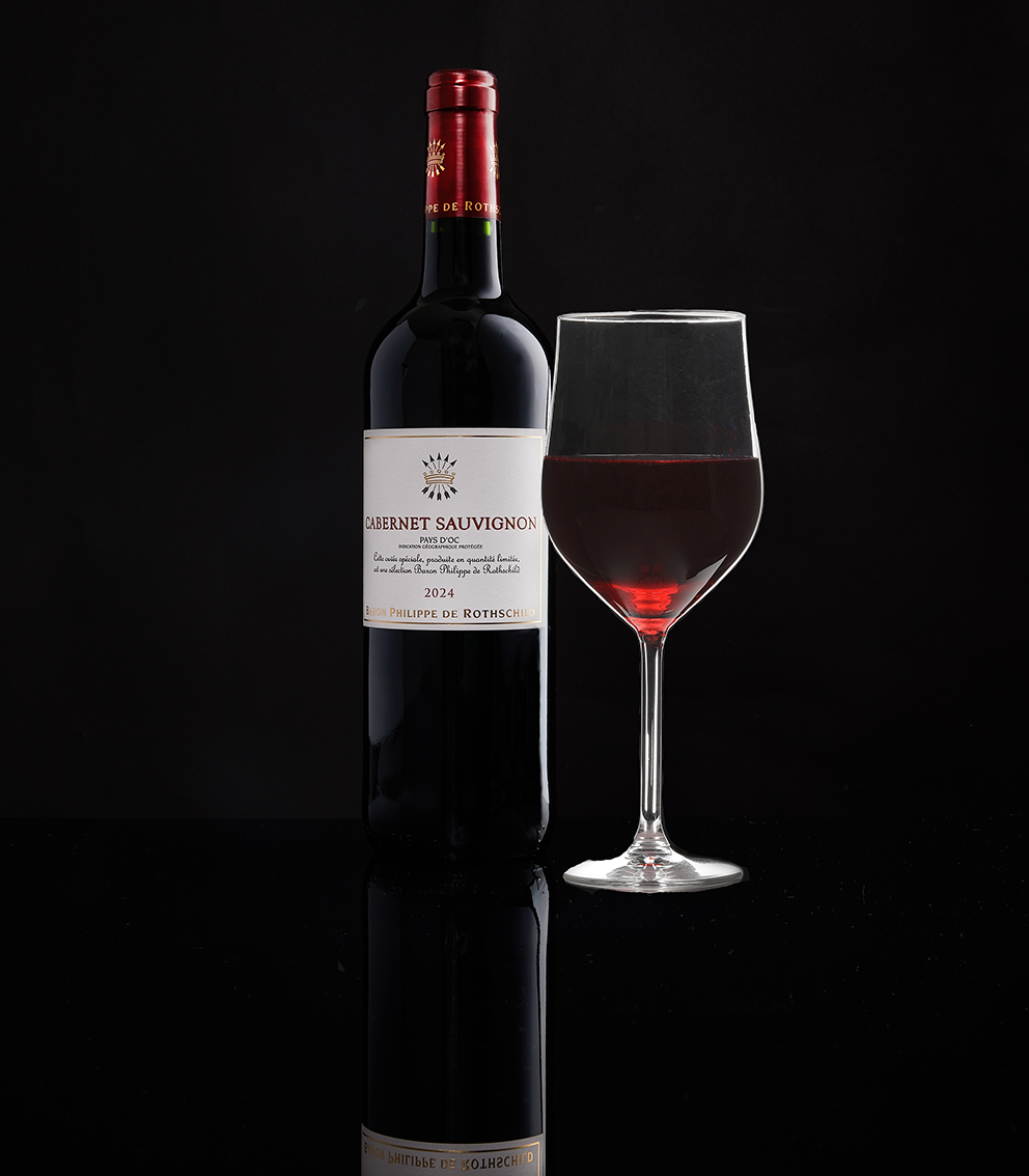 A bottle of Cabernet Sauvignon beside a filled wine glass on a reflective black surface