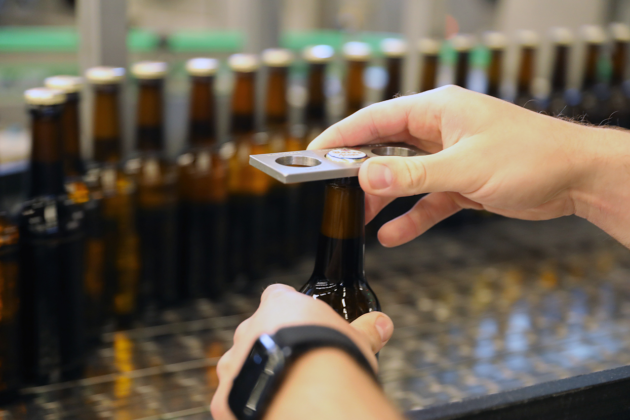 A hand checking the crown cap of a freshly filled bottle at the Barre bottling line